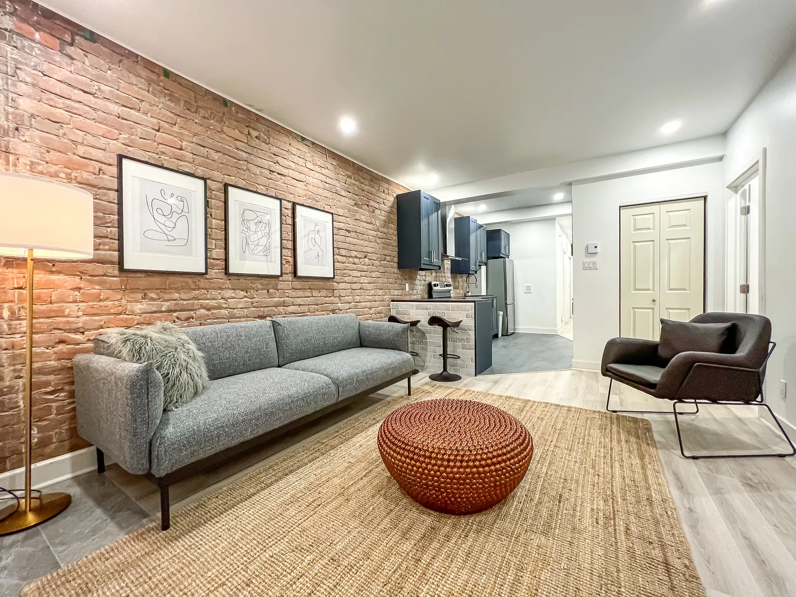 Living room with exposed brick wall, grey sofa and woven pouf
